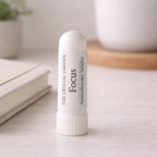 A white cylindrical aromatherapy inhaler labeled 'The Crystal Garden Focus Aromatherapy Inhaler' standing upright on a light wooden surface with a softly blurred background.