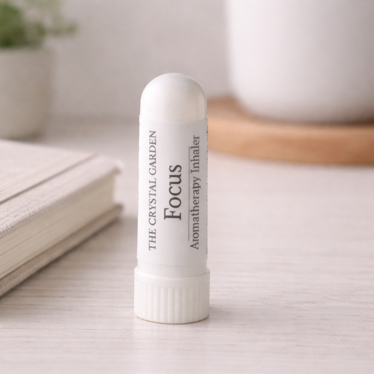 A white cylindrical aromatherapy inhaler labeled 'The Crystal Garden Focus Aromatherapy Inhaler' standing upright on a light wooden surface with a softly blurred background.