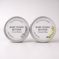 Two round silver metal tins of Baby Tushy Butter by The Crystal Garden, shown side by side on a white background. The left tin is labeled Cocoa Butter with purple lavender illustrations, and the right tin is labeled Vanilla Bean with yellow flower illustrations.