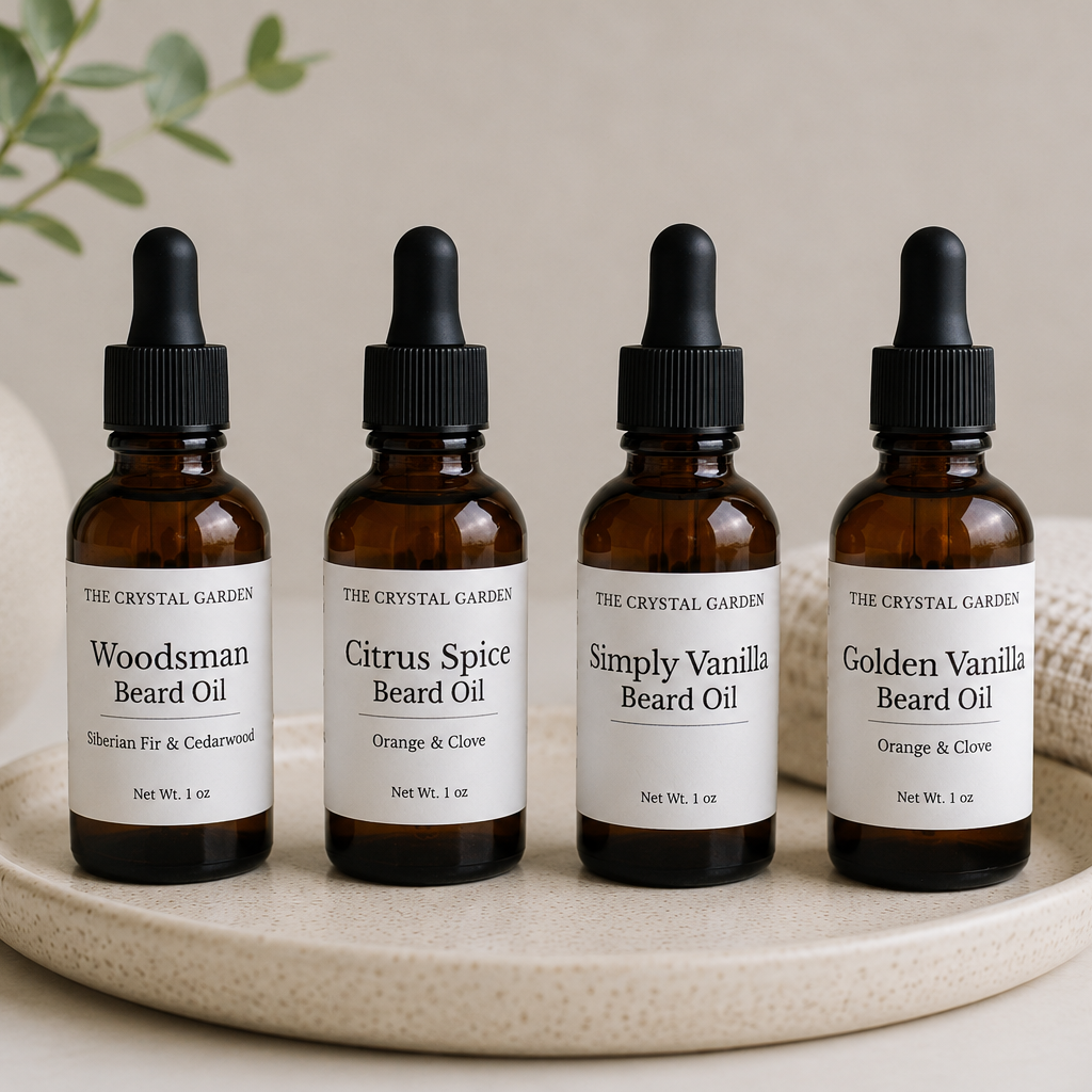 Four amber glass beard oil bottles with black dropper caps arranged on a round beige tray. The labels read The Crystal Garden and include Woodsman, Citrus Spice, Simply Vanilla, and Golden Vanilla.
