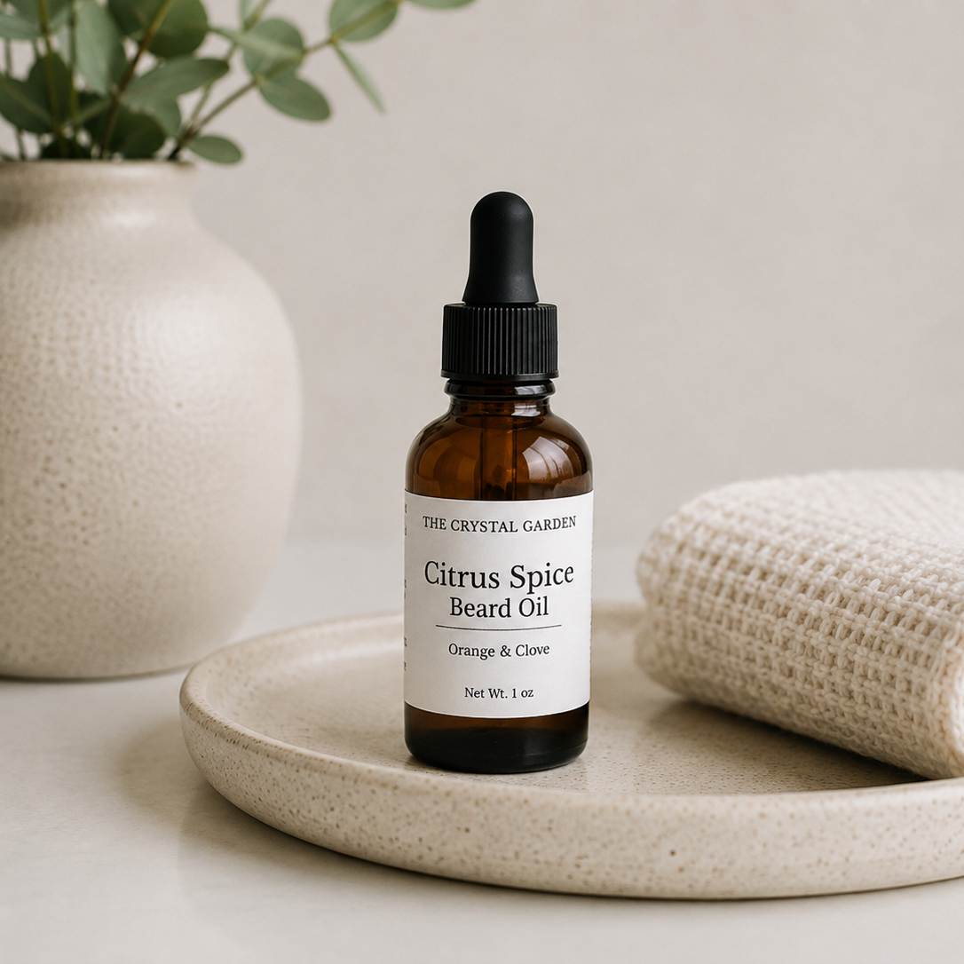 A small amber glass dropper bottle labeled 'The Crystal Gardens Citrus Spice Beard Oil' sits on a round beige tray, styled with a folded cream towel and a ceramic vase in the background.