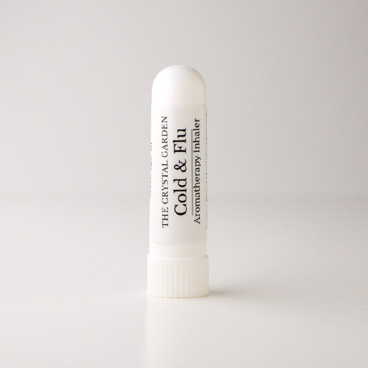 A white plastic cold and flu aromatherapy inhaler tube by The Crystal Garden, standing upright on a light gray background.