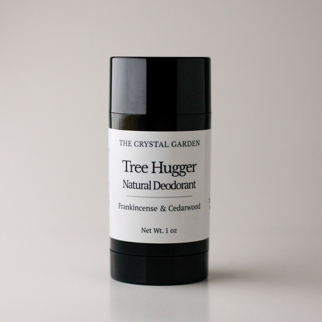 A single stick deodorant container from The Crystal Garden, named Tree Hugger, in Frankincense & Cedarwood scent. The product features a matte black plastic stick with a white paper label, set against a clean, light gray studio background.