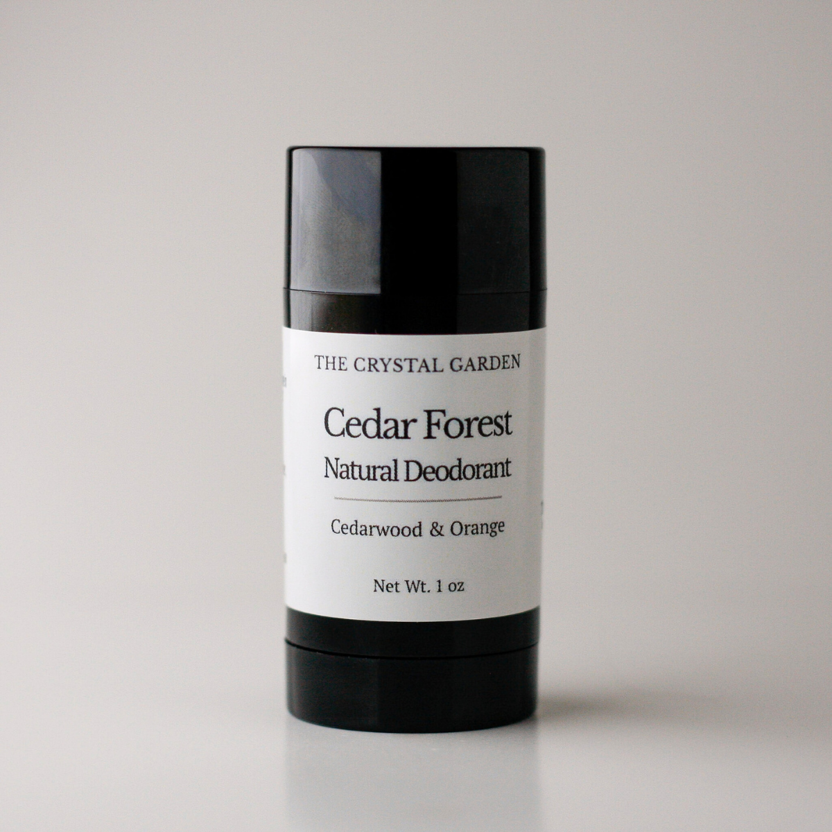 A 1 oz stick deodorant from The Crystal Garden in the Cedar Forest scent, featuring a black container with a white label, set against a neutral light gray background.
