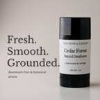 A black cylindrical deodorant stick with a white label reading 'THE CRYSTAL GARDEN Cedar Forest Natural Deodorant' stands on a light gray surface against a pale gray background. Large text on the left reads 'Fresh. Smooth. Grounded aluminum-free and botanical aroma.