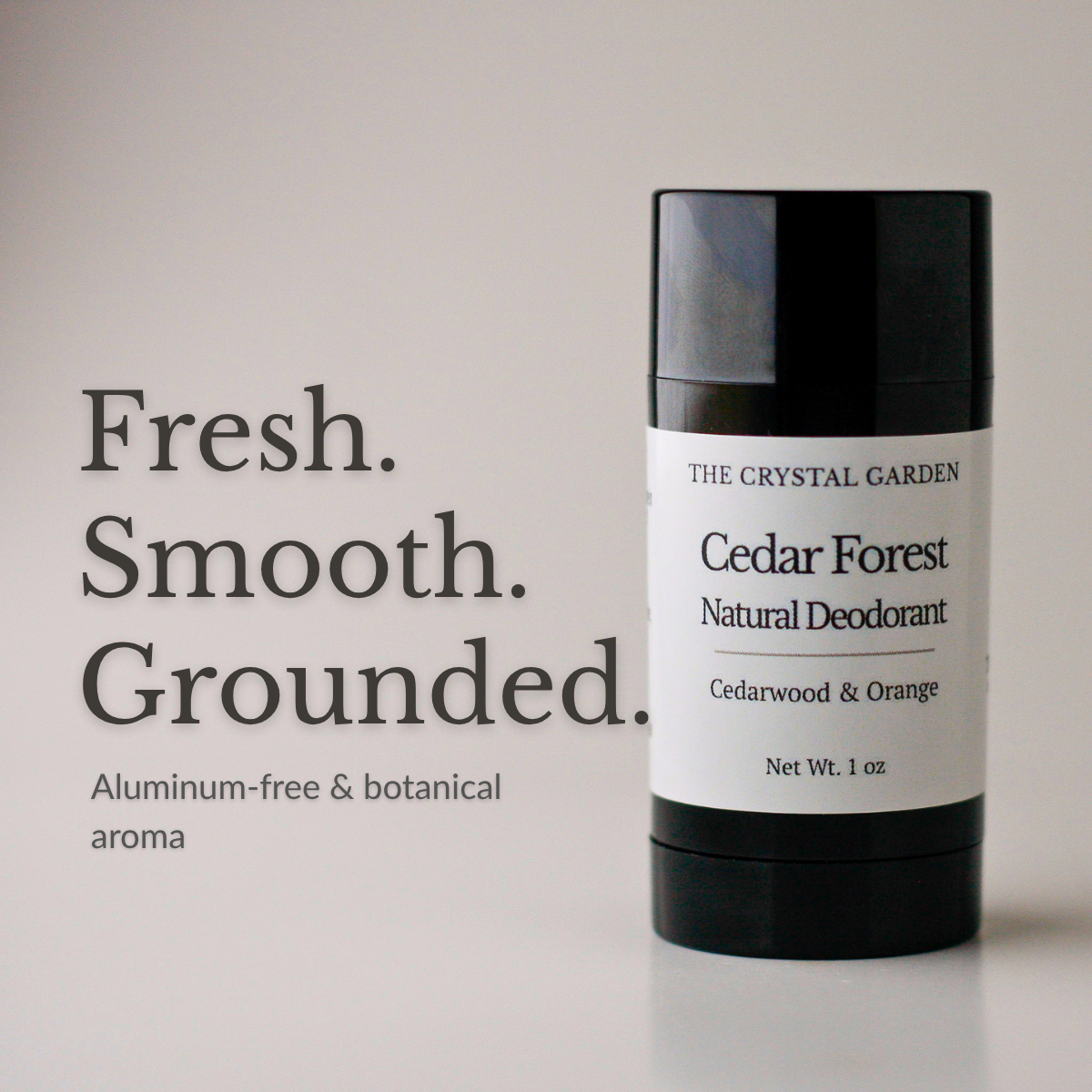 A black cylindrical deodorant stick with a white label reading 'THE CRYSTAL GARDEN Cedar Forest Natural Deodorant' stands on a light gray surface against a pale gray background. Large text on the left reads 'Fresh. Smooth. Grounded aluminum-free and botanical aroma.