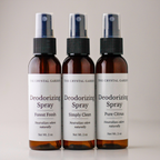 Three amber glass deodorizing spray bottles with white labels and black spray tops, arranged side by side on a light neutral background. The labels read 'The Crystal Garden' and 'Deodorizing Spray' with scent variants Forest Fresh, Simply Clean, and Pure Citrus.