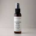 A 2 oz amber glass spray bottle of The Crystal Garden Deodorizing Spray in Pure Citrus scent, featuring a white label and black spray nozzle, set against a neutral gray background.