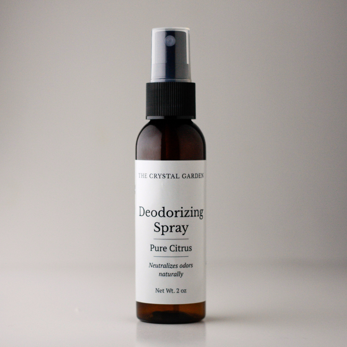 A 2 oz amber glass spray bottle of The Crystal Garden Deodorizing Spray in Pure Citrus scent, featuring a white label and black spray nozzle, set against a neutral gray background.