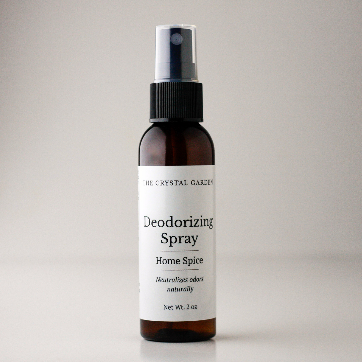 A 2 oz amber glass spray bottle of The Crystal Garden Deodorizing Spray with a white label and black spray nozzle, set against a neutral light gray background.