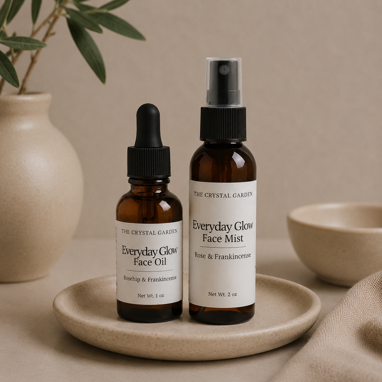 Two amber skincare bottles from The Crystal Garden, one face oil with a dropper and one face mist with a spray top, displayed on a beige ceramic dish with neutral props.