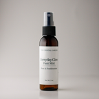 A 2 oz amber spray bottle of The Crystal Garden Everyday Glow Face Mist with Rose & Frankincense, featuring a white label and black spray nozzle, set against a neutral gray background.