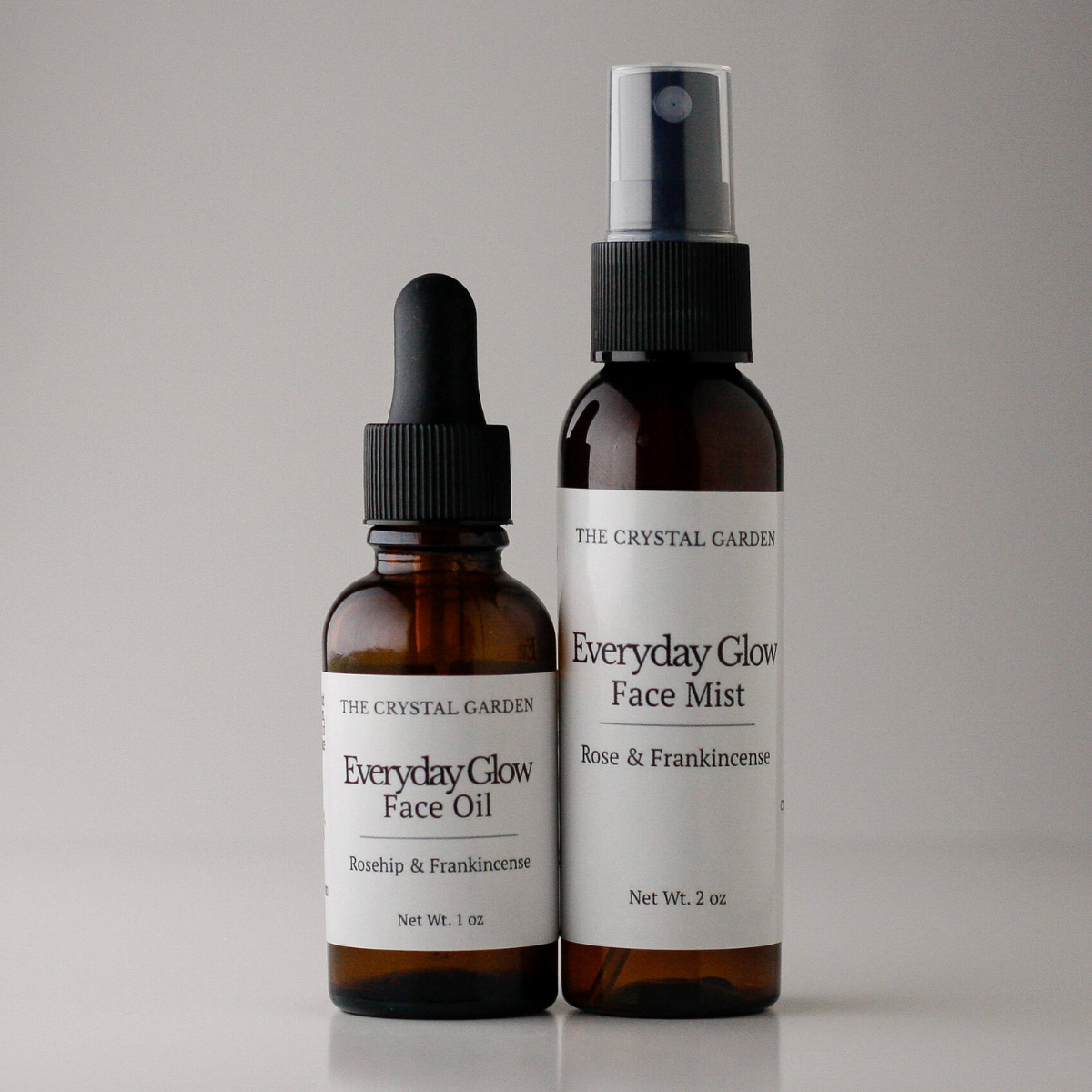 Two amber skincare bottles on a light gray background: a dropper bottle labeled Everyday Glow Face Oil and a spray bottle labeled Everyday Glow Face Mist, both with white labels and black caps.