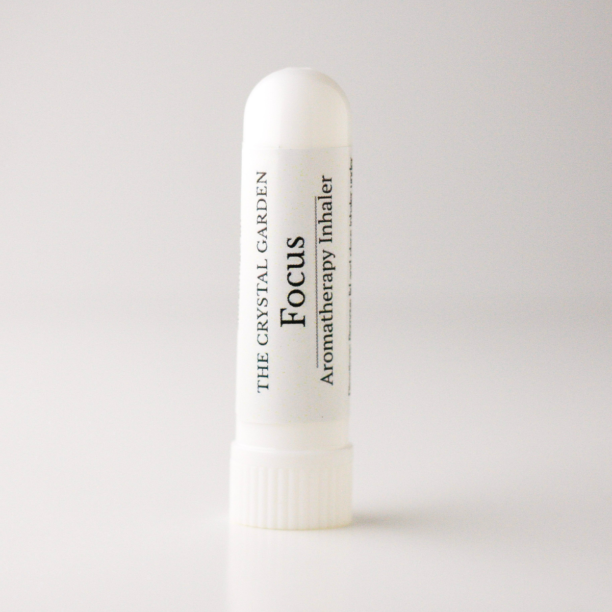 A white cylindrical aromatherapy inhaler tube with a ribbed cap, featuring a white label with black text that reads 'THE CRYSTAL GARDEN Focus Aromatherapy Inhaler'.