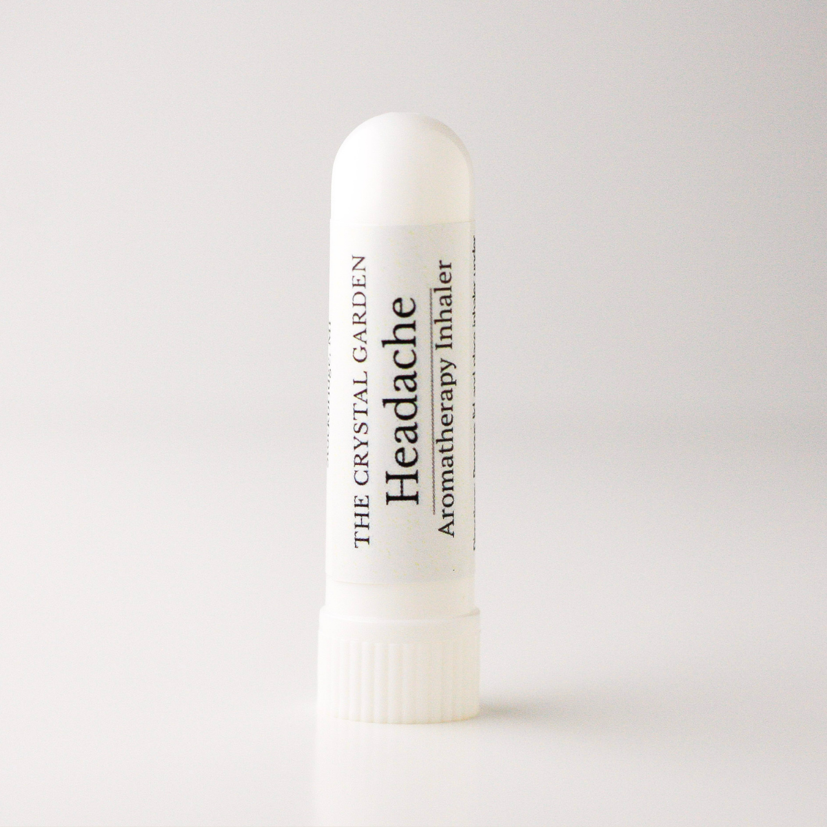 A white cylindrical tube of 'Headache' aromatherapy inhaler by The Crystal Garden, standing upright on a clean white background.
