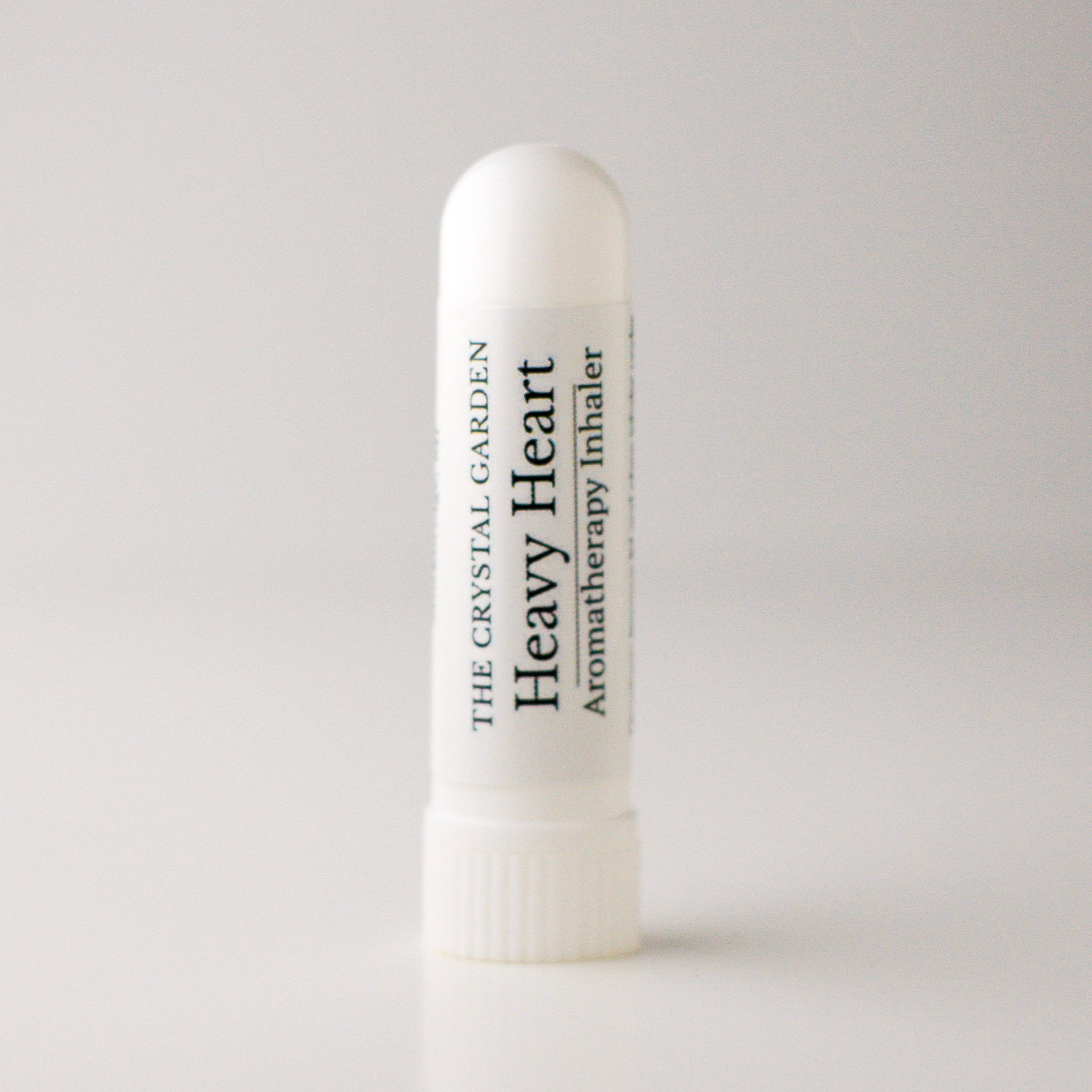 A white cylindrical aromatherapy inhaler tube standing upright on a light gray background. The label reads 'THE CRYSTAL GARDEN Heavy Heart Aromatherapy Inhaler' in black text.