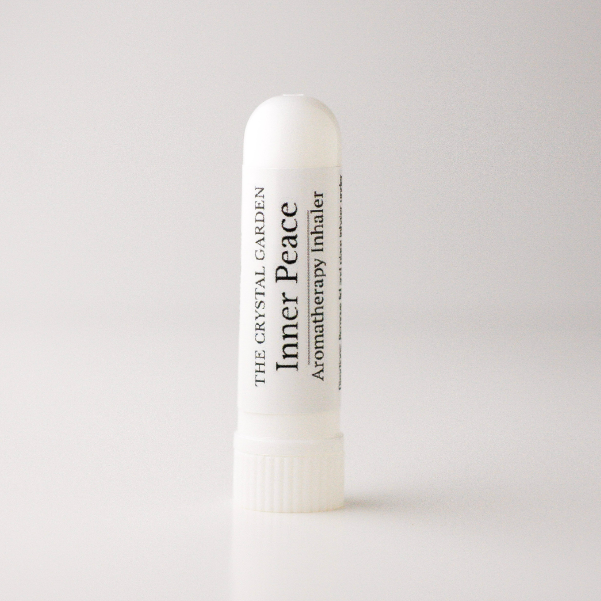 A white plastic aromatherapy inhaler tube standing upright on a light gray background. The label reads 'THE CRYSTAL GARDEN' and 'Inner Peace Aromatherapy Inhaler'.