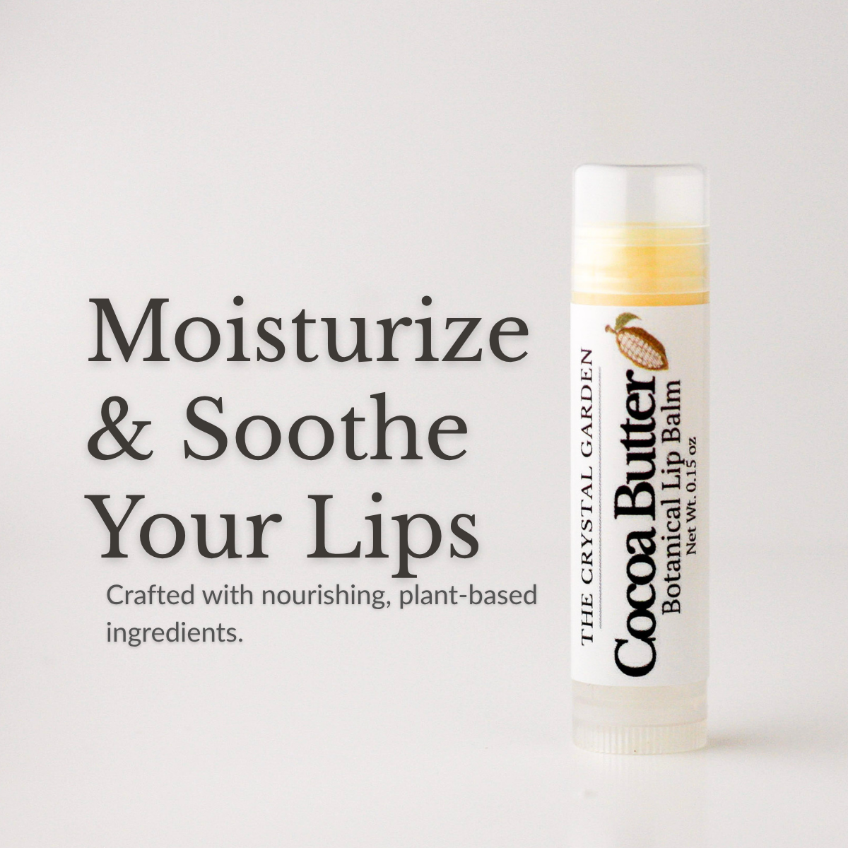 A tube of The Crystal Garden Cocoa Butter Botanical Lip Balm stands on a light gray background next to promotional text that reads 'Moisturize & Soothe Your Lips.'.