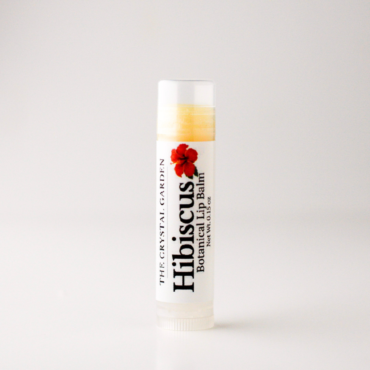 A single tube of lip balm standing upright on a plain light background. The label reads 'The Crystal Garden' and 'Hibiscus Botanical Lip Balm,' with a red hibiscus flower graphic on a white tube.