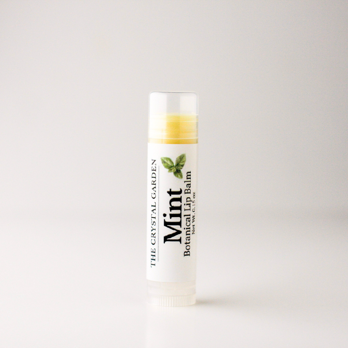 A single tube of mint botanical lip balm from The Crystal Garden, standing upright on a clean white surface against a light gray background.