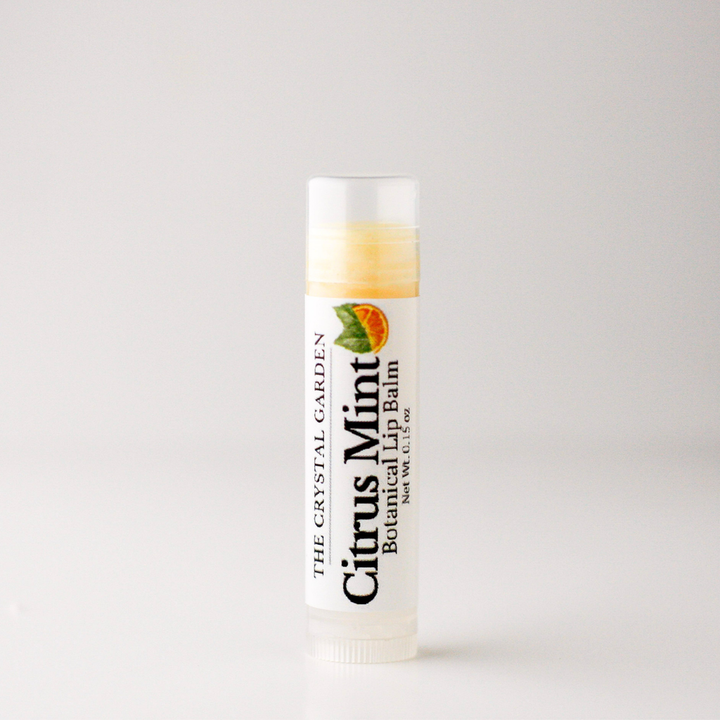A tube of 'Citrus Mint Botanical Lip Balm' by 'The Crystal Garden' standing upright on a light gray background.