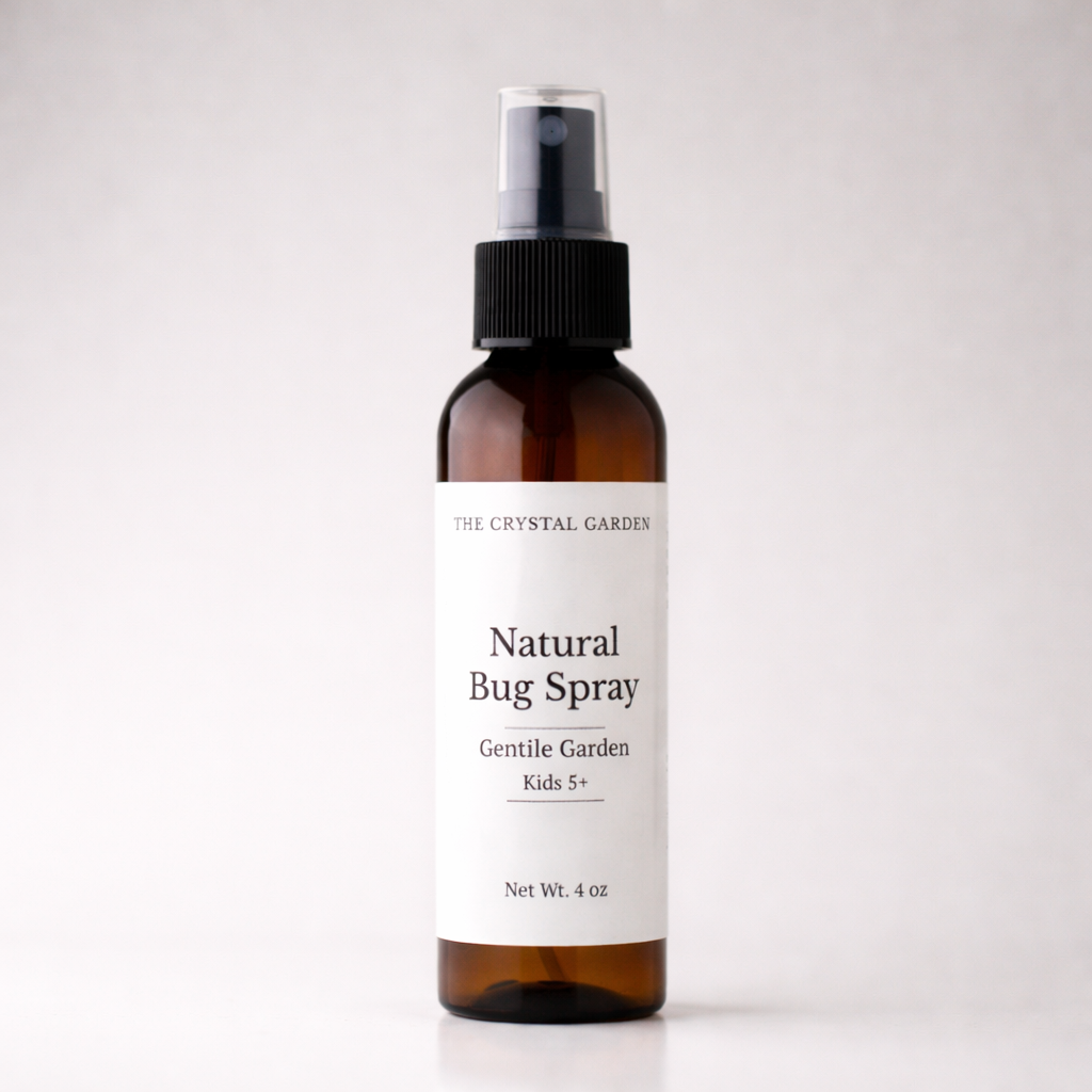 An amber glass spray bottle of The Crystal Garden Natural Bug Spray with a white label and black spray nozzle, set against a light gray background.