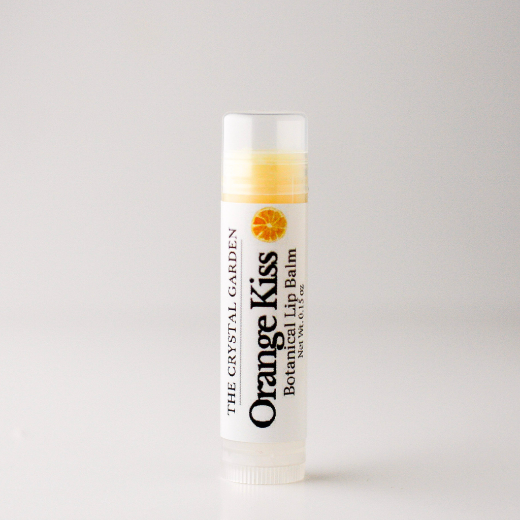 A single tube of lip balm standing upright on a plain light background. The label reads 'Orange Kiss Botanical Lip Balm' with 'The Crystal Garden' branding and an orange slice graphic.
