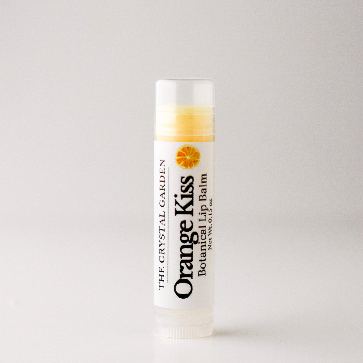A single tube of lip balm standing upright on a plain light background. The label reads 'Orange Kiss Botanical Lip Balm' with 'The Crystal Garden' branding and an orange slice graphic.