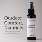 An amber glass spray bottle of The Crystal Garden Natural Bug Spray with a white label, shown next to promotional text on a light gray background.