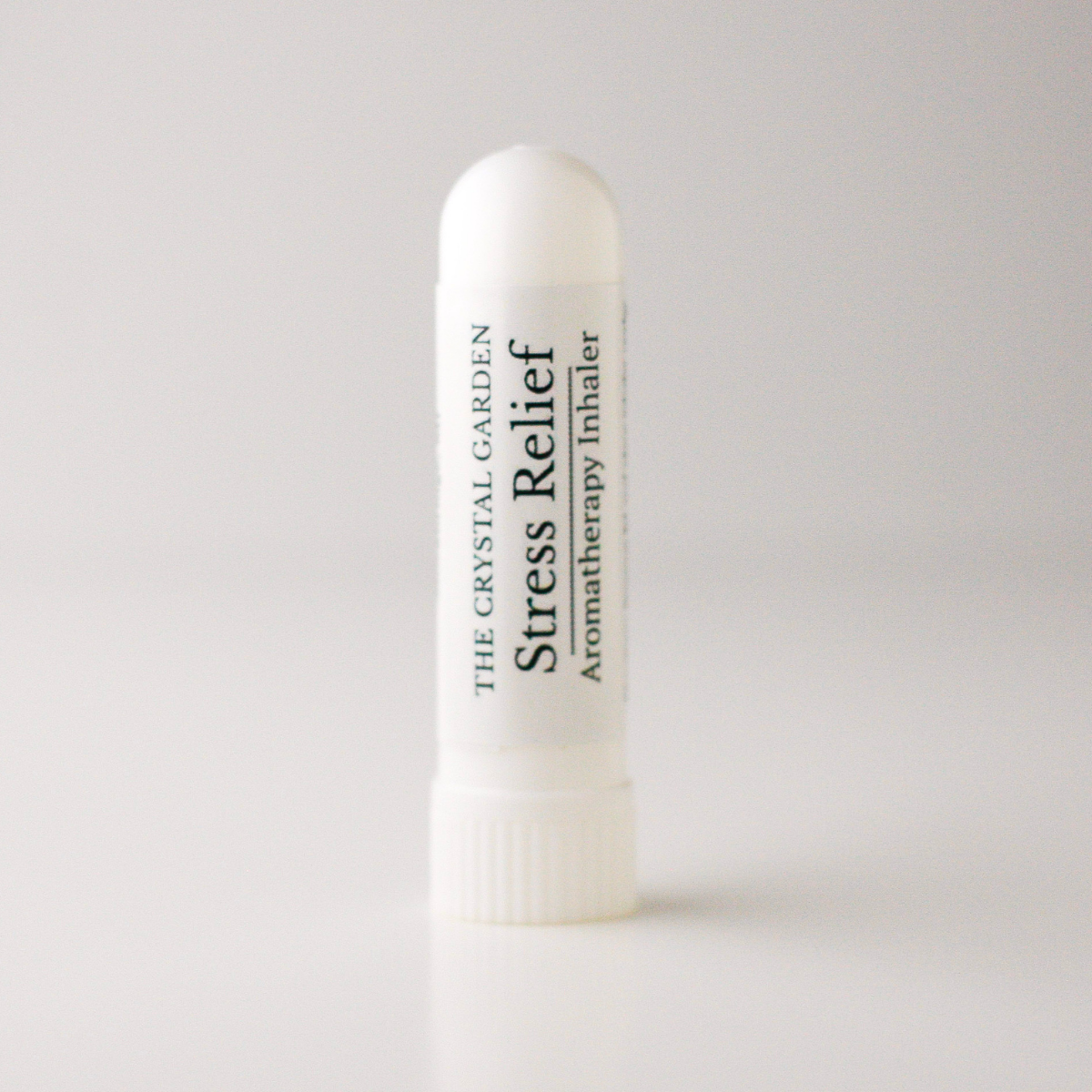 A white cylindrical aromatherapy inhaler tube labeled 'THE CRYSTAL GARDEN Stress Relief Aromatherapy Inhaler' on a light gray background.