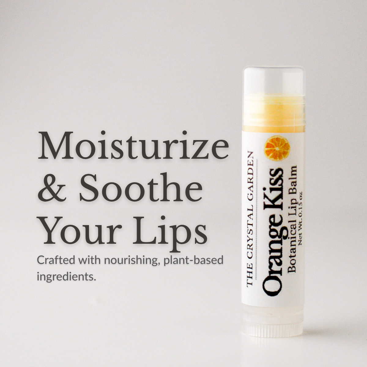 A tube of The Crystal Garden Orange Kiss Botanical Lip Balm stands on a light gray background next to large text that reads 'Moisturize & Soothe Your Lips' and smaller text about plant-based ingredients.