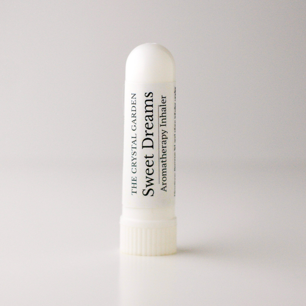 A white cylindrical aromatherapy inhaler tube standing upright on a light gray background. The label reads 'THE CRYSTAL GARDEN Sweet Dreams Aromatherapy Inhaler' in black text.