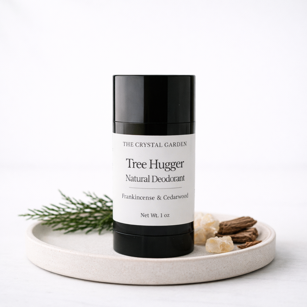 A black and white deodorant stick from The Crystal Garden, styled on a round ceramic tray with green sprigs and dried botanicals against a white background.