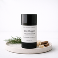 A black and white deodorant stick from The Crystal Garden, styled on a round ceramic tray with green sprigs and dried botanicals against a white background.
