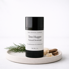 A black and white deodorant stick from The Crystal Garden, styled on a round ceramic tray with green sprigs and dried botanicals against a white background.