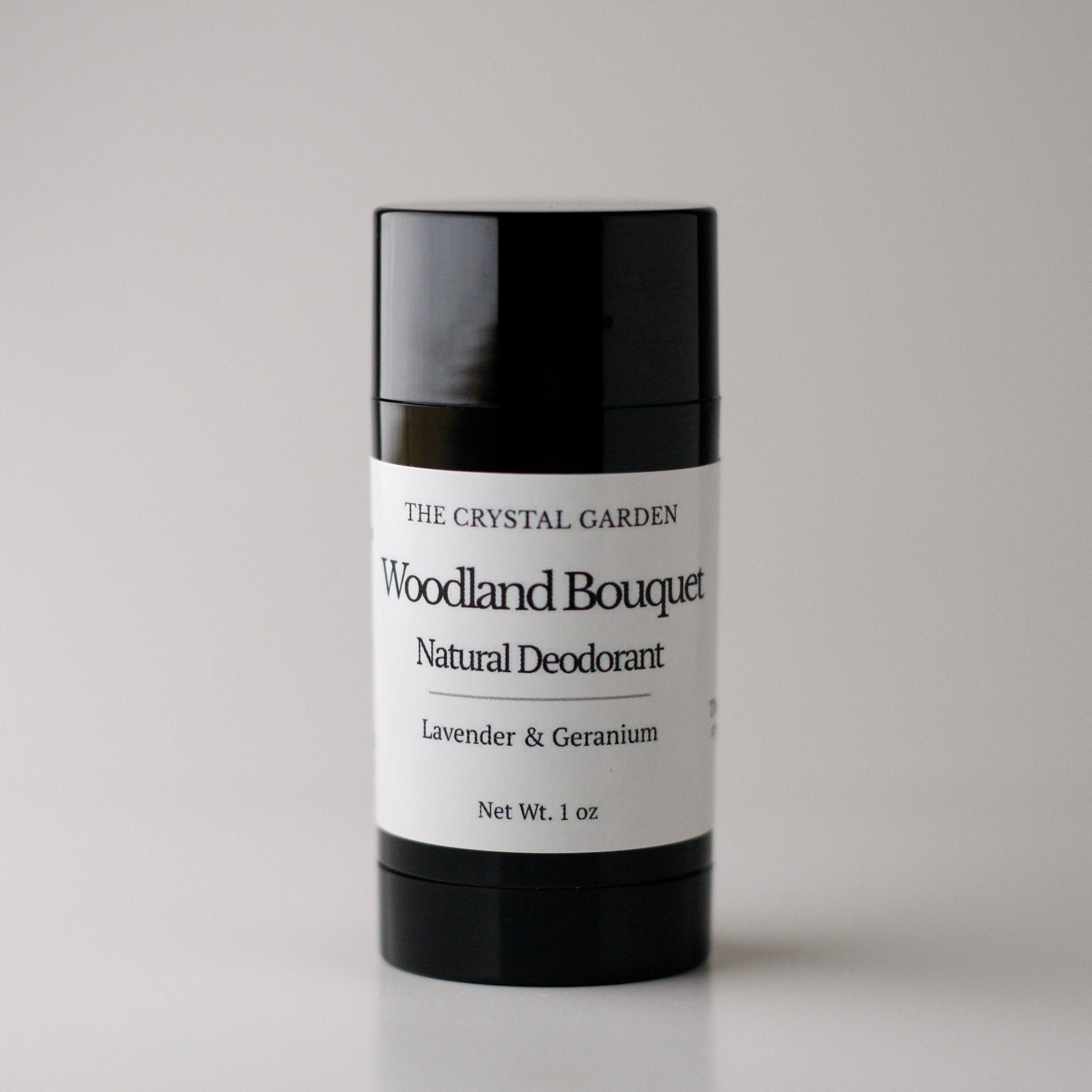 A 1 oz black plastic stick container of The Crystal Garden Woodland Bouquet Natural Deodorant, featuring a white label with black text, set against a neutral light gray background.