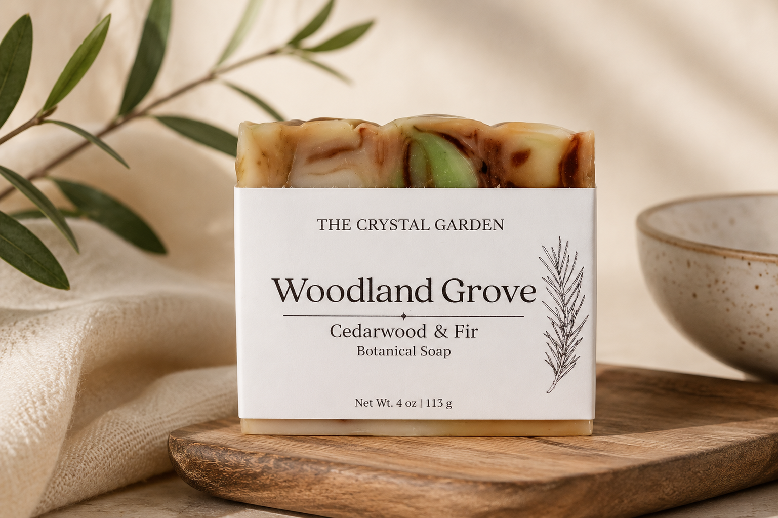 A rectangular bar of soap labeled 'Woodland Grove' by The Crystal Garden, placed on a wooden board with a cream cloth and a ceramic bowl in the background.