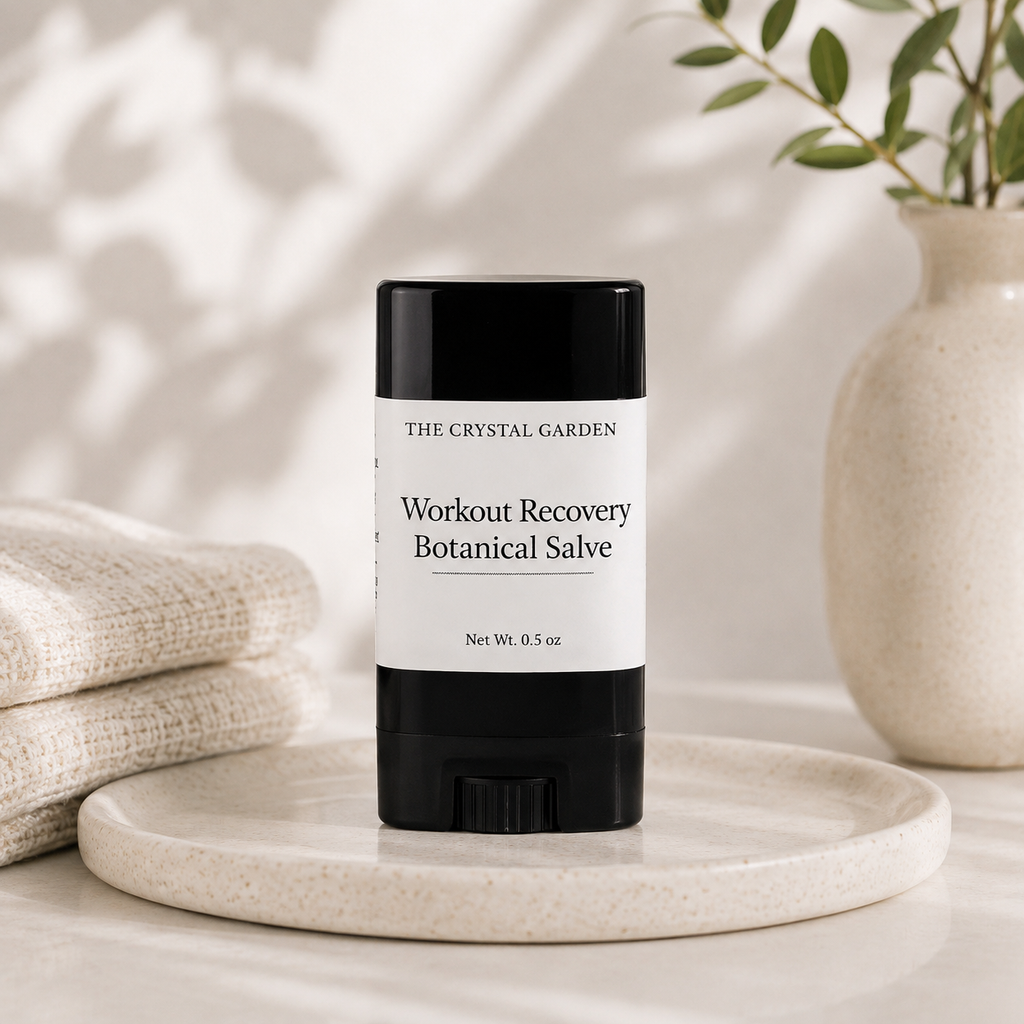 A black and white stick of 'Workout Recovery Botanical Salve' by The Crystal Garden, displayed on a ceramic tray with folded linen and a vase in the background.