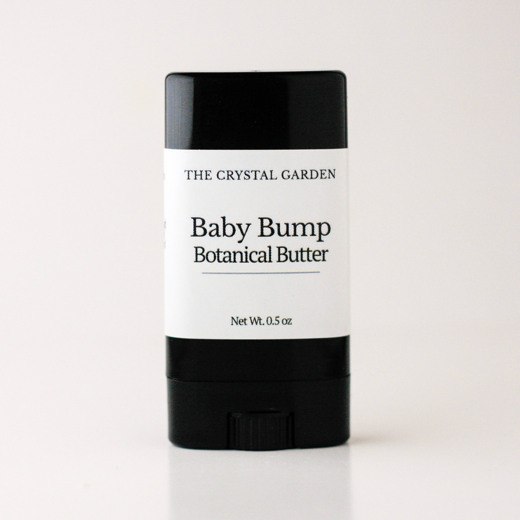 A single stick of baby cream or balm with a black container and a white label reading 'THE CRYSTAL GARDEN Baby Bump Botanical Butter' on a clean white background.