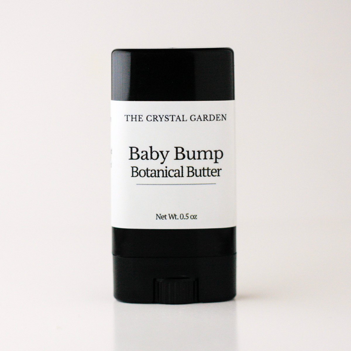 A single stick of baby cream or balm with a black container and a white label reading 'THE CRYSTAL GARDEN Baby Bump Botanical Butter' on a clean white background.
