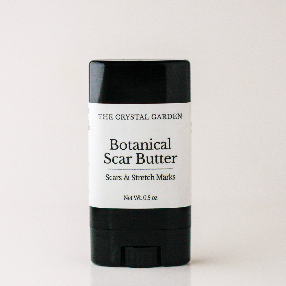 A black and white stick container of The Crystal Garden Botanical Scar Butter, shown on a clean white background.