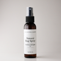 An amber glass spray bottle of 'Natural Bug Spray' by The Crystal Garden, featuring a white label and a black spray nozzle, set against a plain light gray background.
