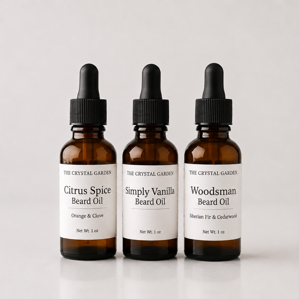 Three amber glass dropper bottles of beard oil from The Crystal Garden, labeled Citrus Spice, Simply Vanilla, and Woodsman, arranged on a light gray background.