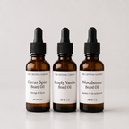Three amber glass dropper bottles of beard oil from The Crystal Garden, labeled Citrus Spice, Simply Vanilla, and Woodsman, arranged on a light gray background.