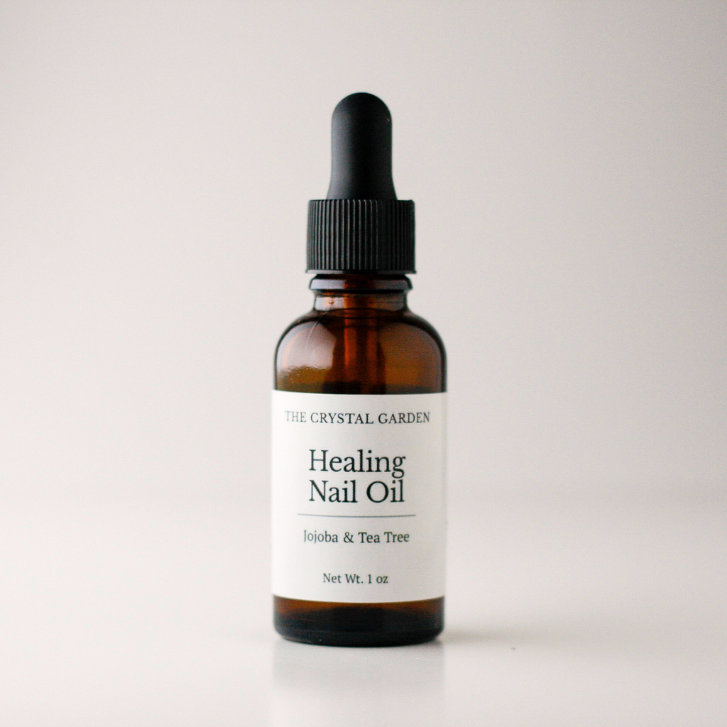 An amber glass dropper bottle of The Crystal Garden Healing Nail Oil on a light gray background.