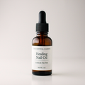 An amber glass dropper bottle of The Crystal Garden Healing Nail Oil on a light gray background.