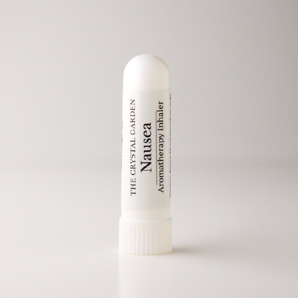 A white cylindrical nasal spray bottle labeled 'Nausea' by The Crystal Garden Aromatherapy Inhaler, standing upright on a light gray background.