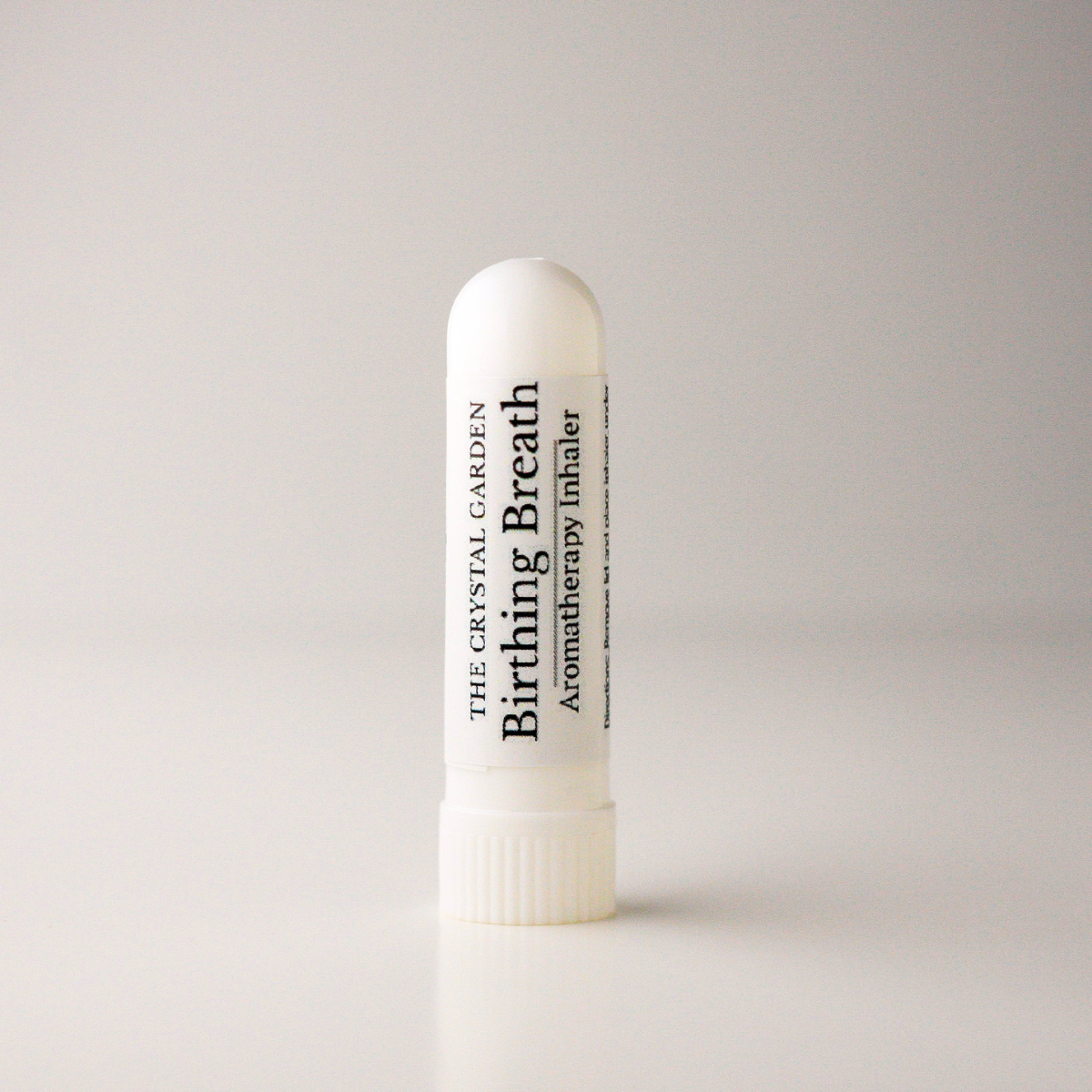 A white cylindrical aromatherapy inhaler tube with a ribbed screw cap, standing upright on a light gray background. The label reads 'THE CRYSTAL GARDEN Birthing Breath Aromatherapy inhaler'.