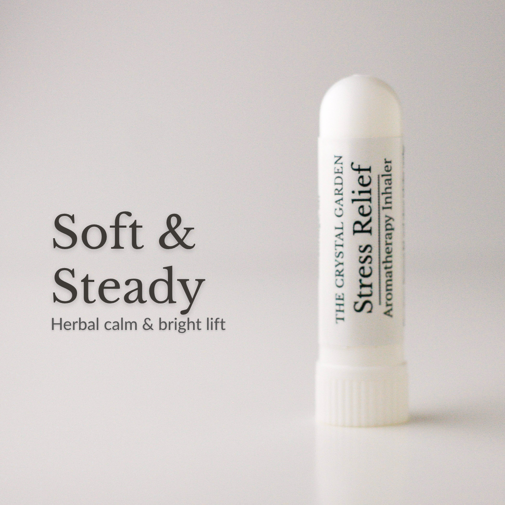 A white cylindrical stress relief aromatherapy inhaler by The Crystal Garden stands on a light gray surface against a light gray background. To the left, large black text reads 'Soft & Steady' with smaller text 'Herbal calm & bright lift'.
