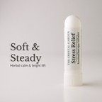 A white cylindrical stress relief aromatherapy inhaler by The Crystal Garden stands on a light gray surface against a light gray background. To the left, large black text reads 'Soft & Steady' with smaller text 'Herbal calm & bright lift'.